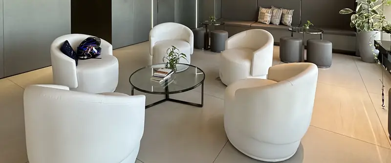 Lounge da clínica com poltronas brancas em volta de uma mesa de vidro.