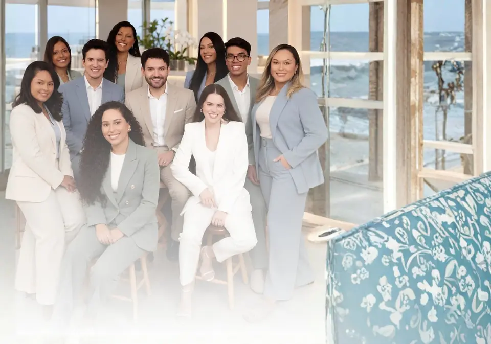 Equipe da Clínica Gadelha reunida, em trajes claros, diante de janelas com vista para o mar.